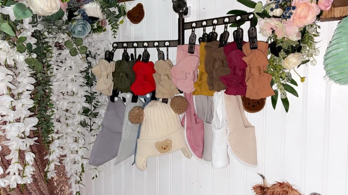 Rompers and knit bear hats hanging on a rail among silk florals.