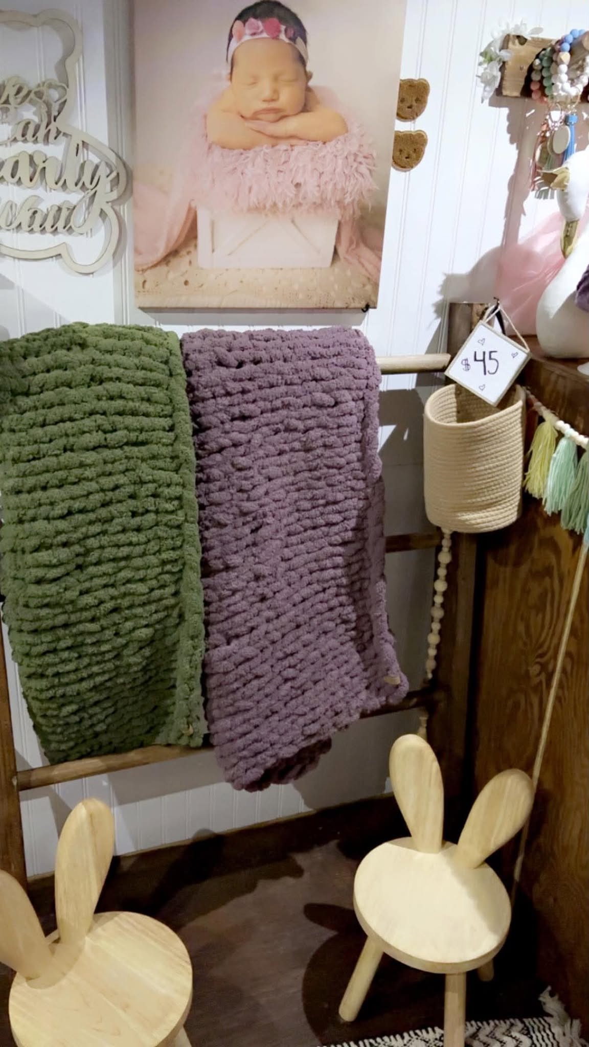 Chunky knit blankets in sage and plum hanging on a wooden ladder.