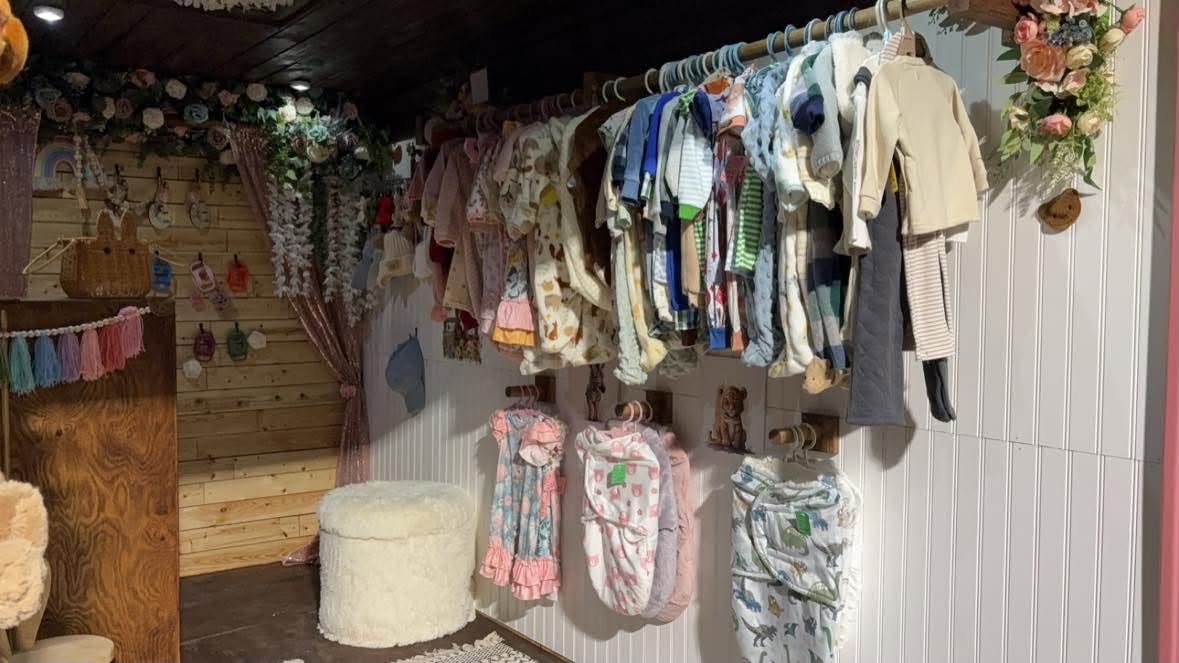 Rails of tiny baby clothes beneath silk florals and fairy lights.