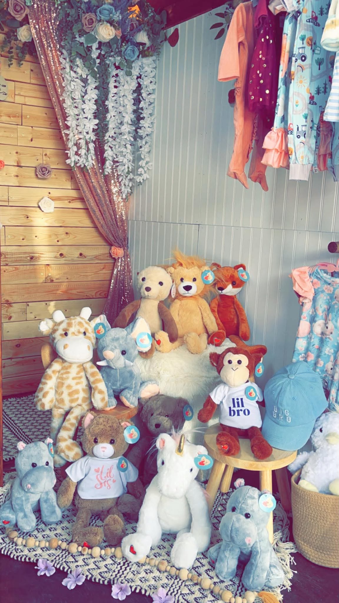 A corner of the boutique with plush animals gathered on a rug beneath hanging outfits.