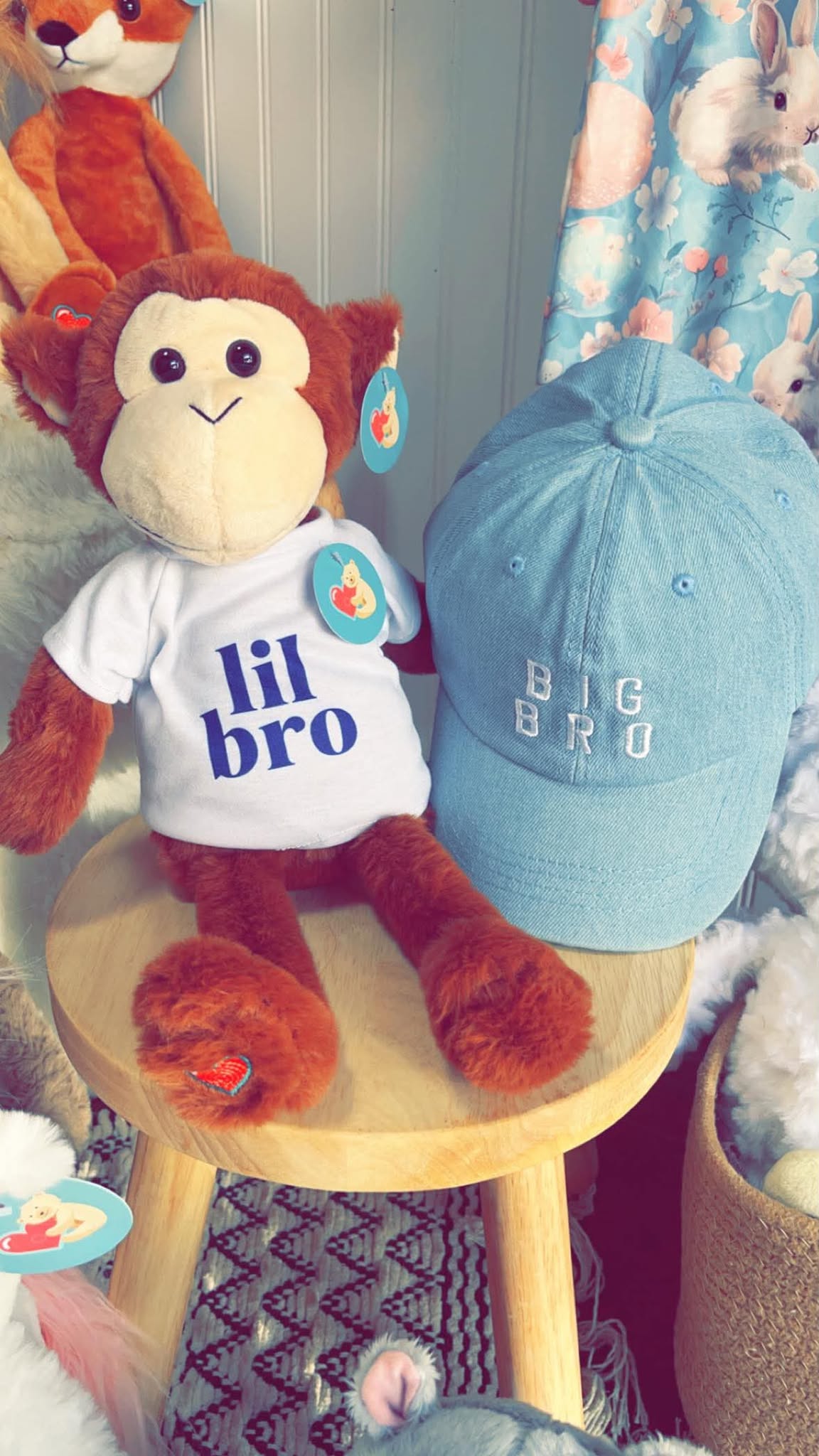 A plush monkey in a lil bro shirt beside a denim big bro cap.